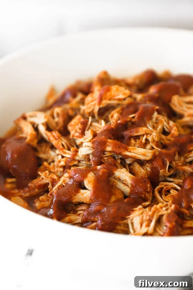 Close up angle of shredded chicken in a bowl topped with bbq sauce
