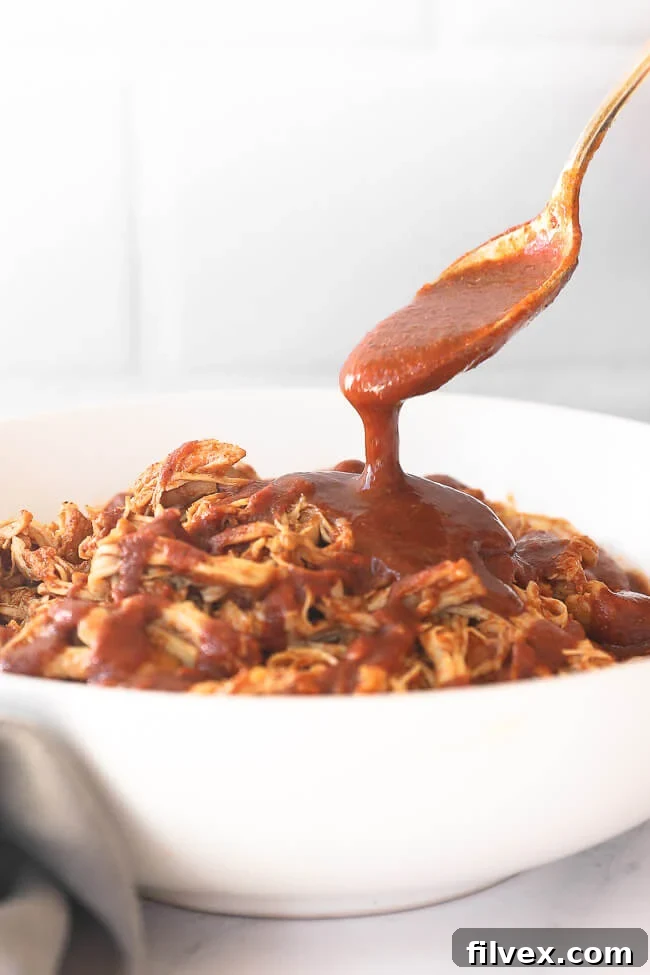 Shredded chicken in a bowl with a spoon pouring BBQ sauce on top