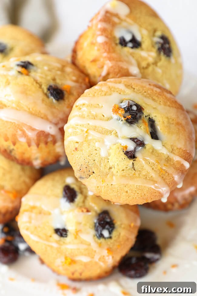 Angled shot of two stacked gluten-free orange cranberry muffins on a white plate, generously drizzled with a dairy-free orange icing.