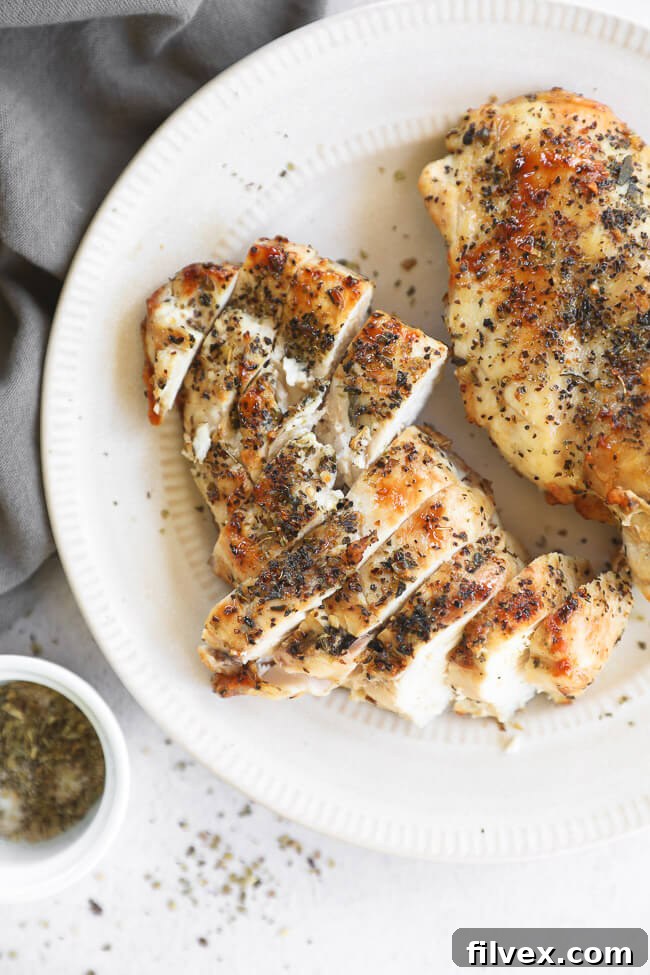 Two cooked air fryer chicken breasts on a plate. One breast sliced up.
