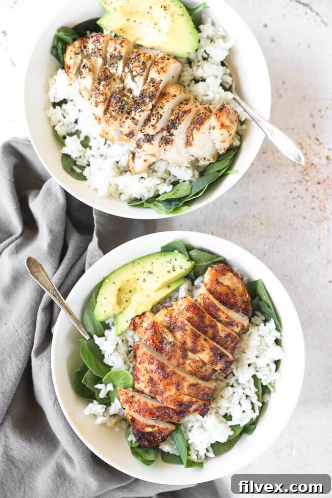 Two bowls of sliced chicken breasts over greens and rice with avocado