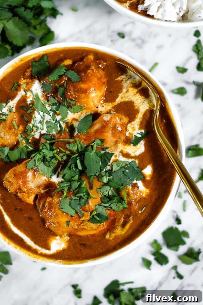 A bowl of delicious Instant Pot butter chicken, garnished with fresh chopped cilantro, next to a spoon.