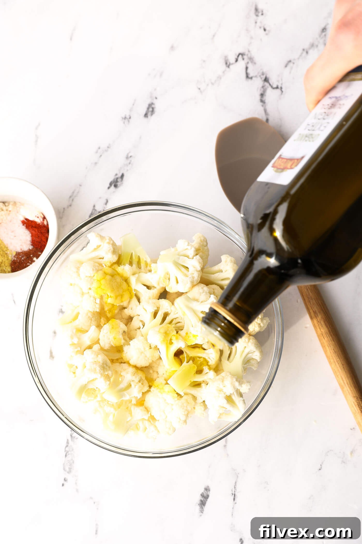 Melted ghee being drizzled over cauliflower florets in a bowl, before tossing.