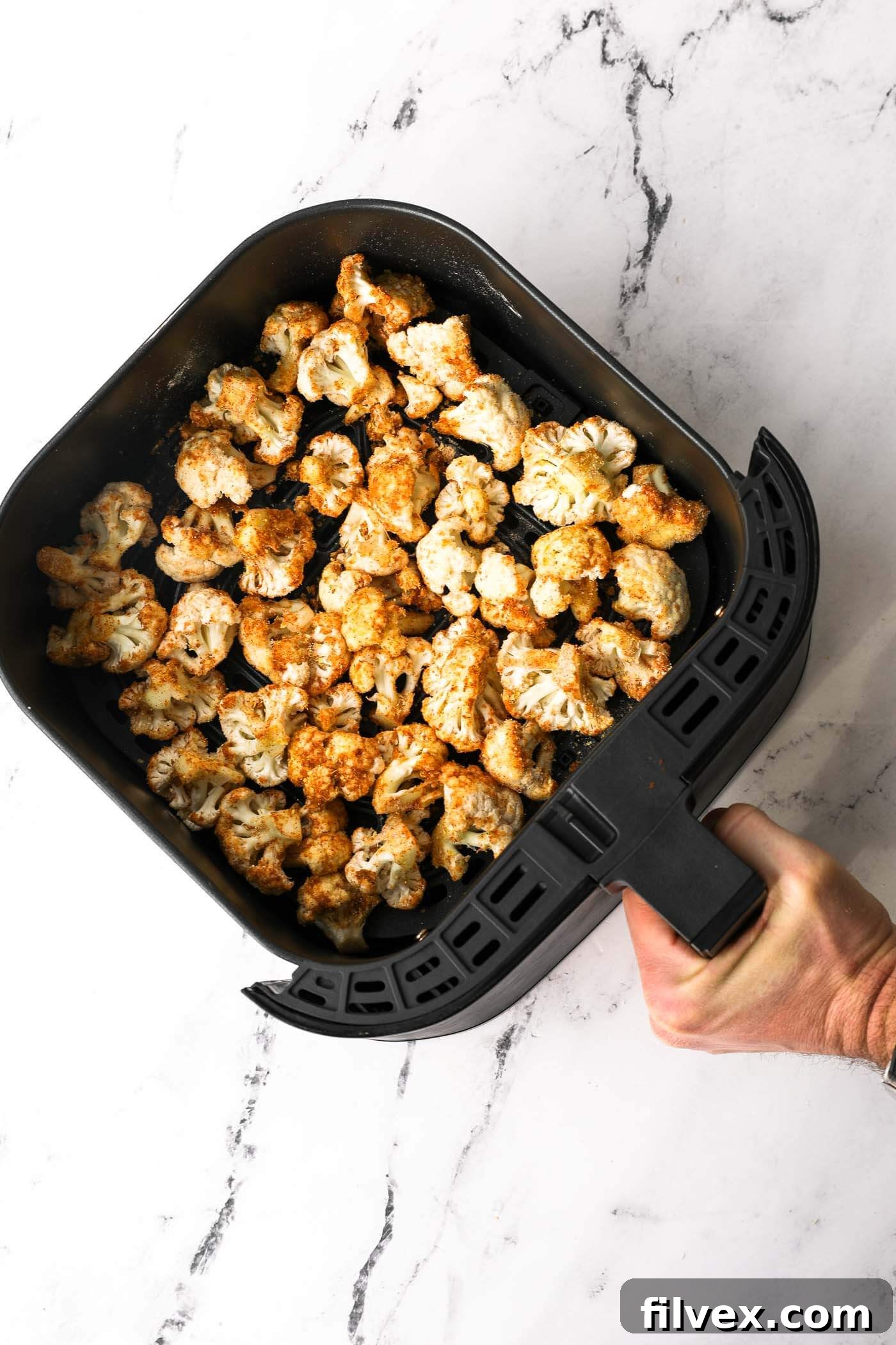 Seasoned cauliflower florets arranged in a single layer inside an air fryer basket.