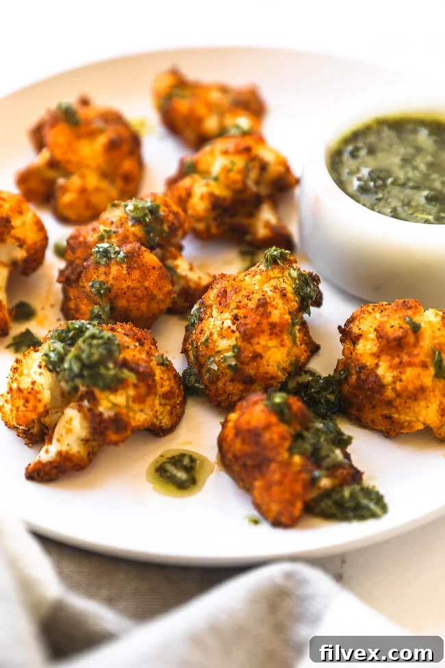 Close-up angled shot of crispy air fryer cauliflower on a white plate, garnished with fresh green sauce and a lime wedge.