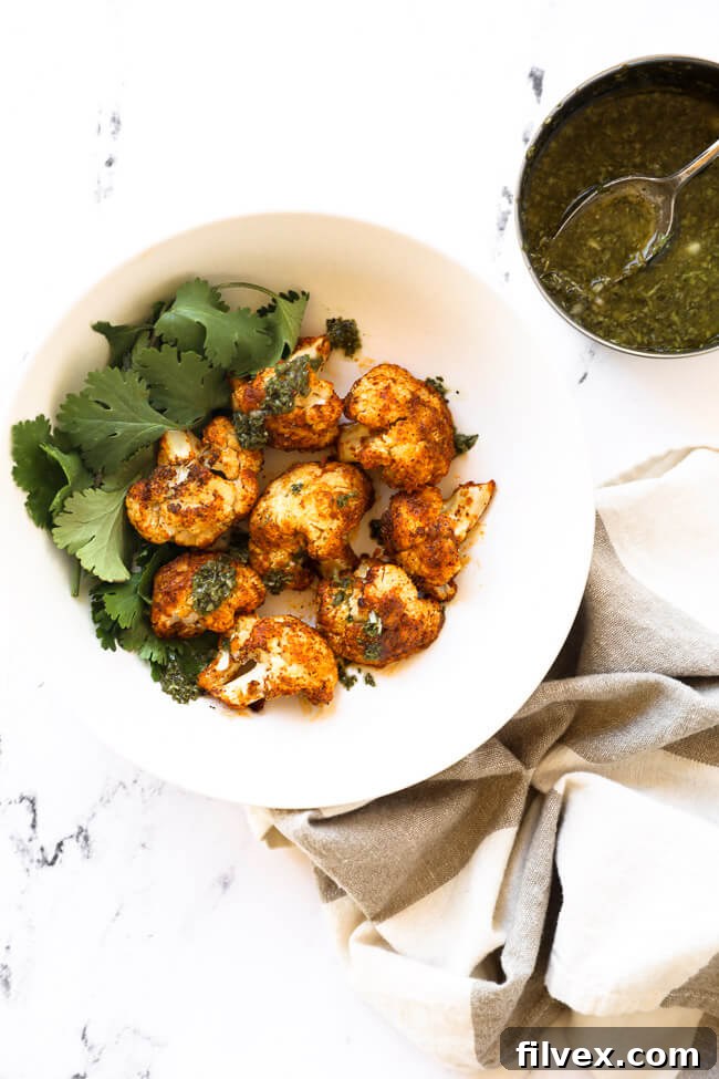 A bowl filled with perfectly cooked air fryer cauliflower, garnished with fresh parsley, with a small dish of green sauce on the side.