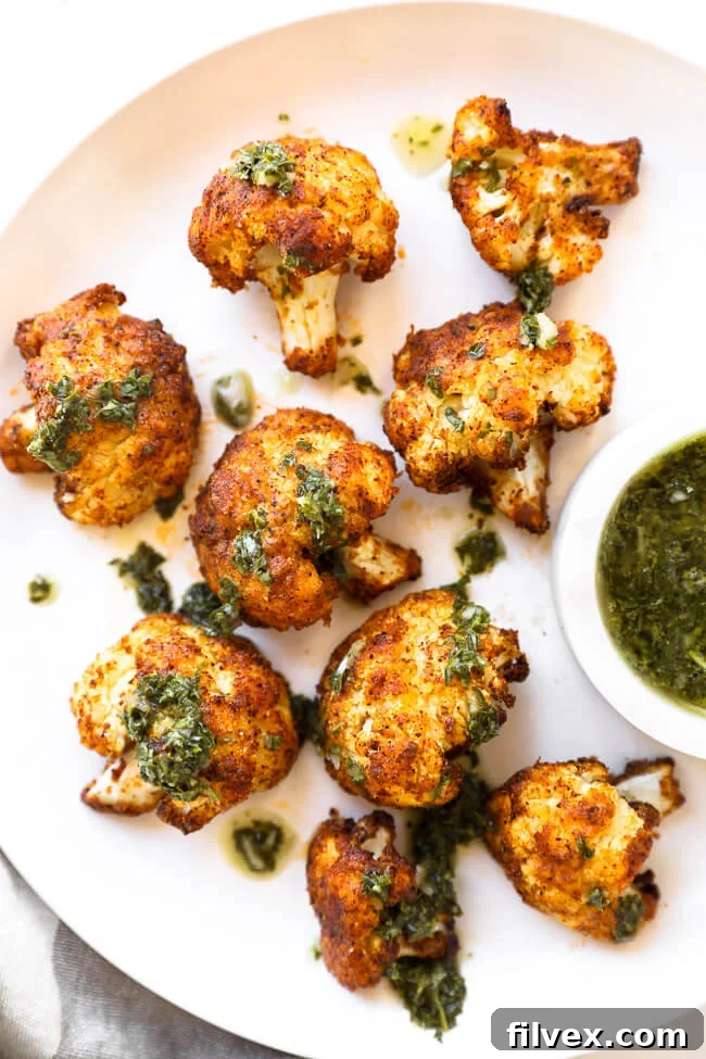 Crispy air fryer cauliflower presented beautifully on a white plate, featuring green sauce both on top and as a dipping option on the side.