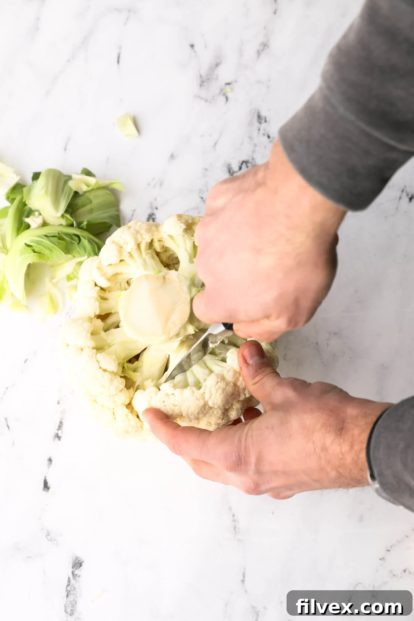 A sharp knife carefully cutting florets away from the main stem of the cauliflower.