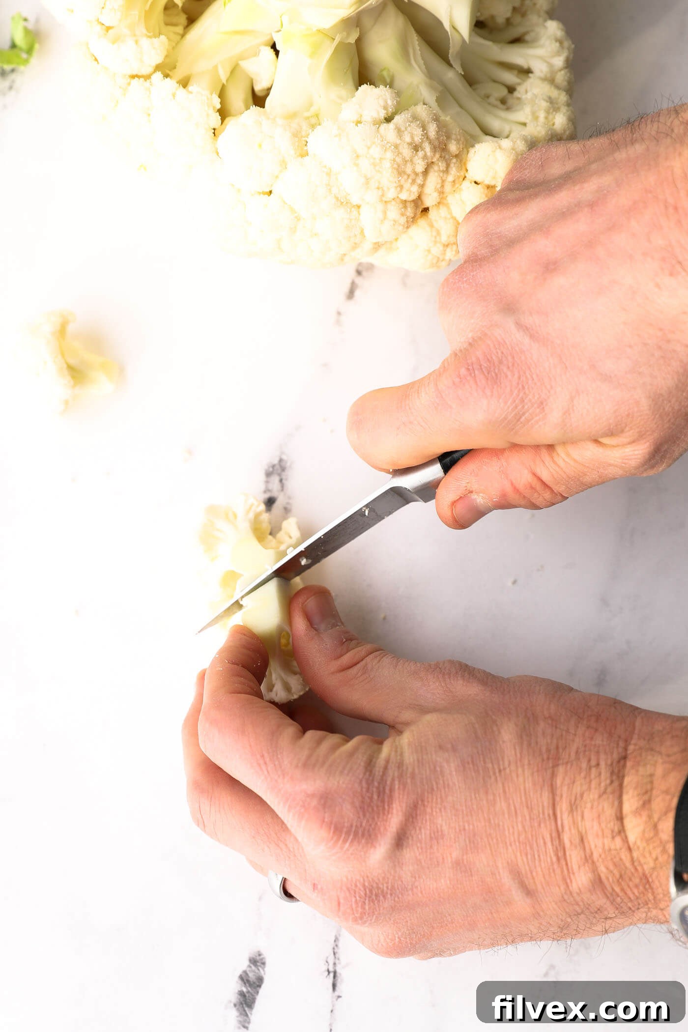 A knife cutting cauliflower florets into smaller, more uniform pieces for cooking.