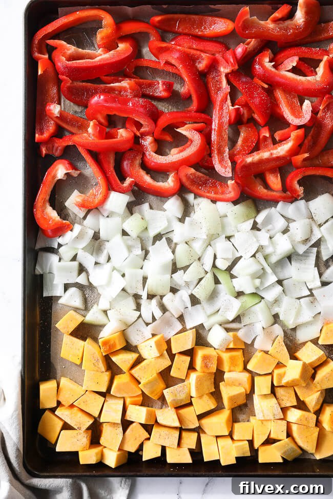 A sheet pan with chopped red bell peppers, onion and butternut squash. 
