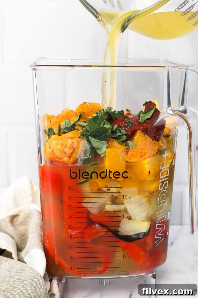 Blender with all of the soup ingredients in it and broth being poured in before blending. 