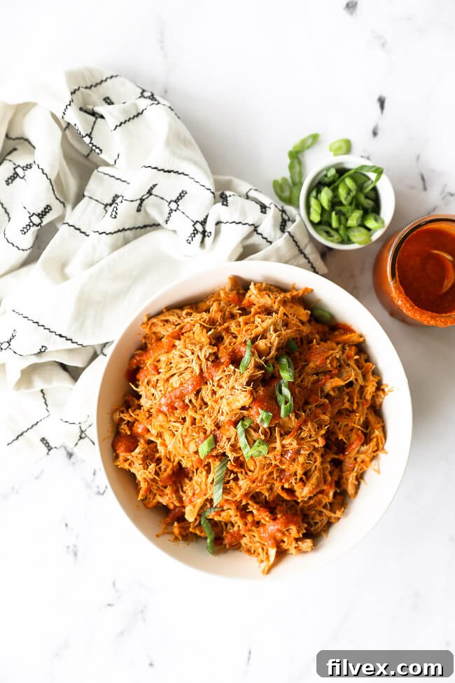 Instant pot buffalo chicken shredded in a bowl with sliced green onions on top and sauce and onions on the side