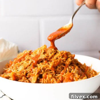 Bowl of shredded instant pot buffalo chicken with sauce pouring in from a spoon
