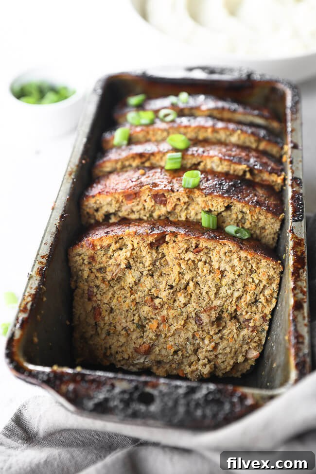 Close up angle image of chicken meatloaf slices in a loaf pan with green onion on top