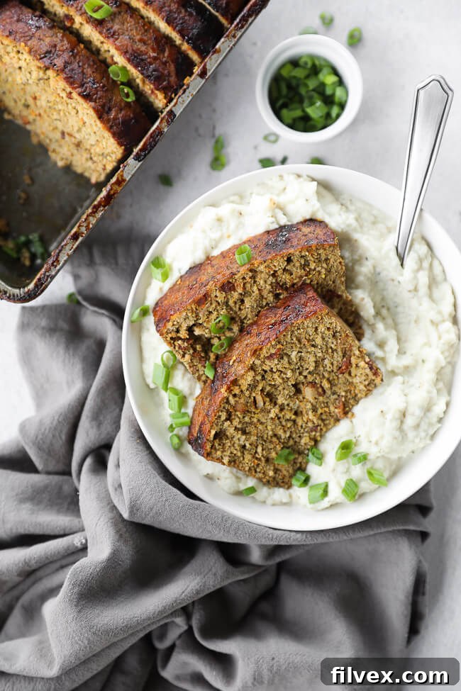 Two slices of chicken meatloaf over a bowl filled with mashed potatoes and a spoon coming out