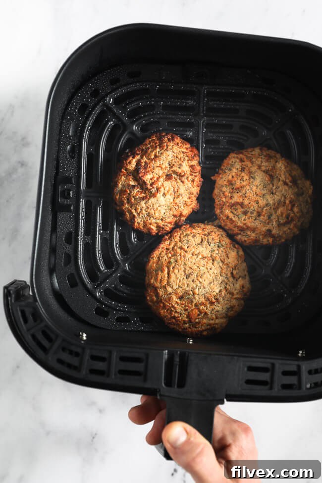 Three cooked salmon patties in an air fryer basket with hand holding basket