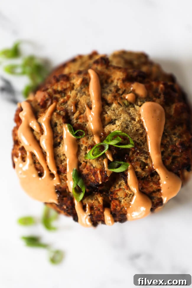 Single salmon patty with a drizzle of orange sauce on top and sliced green onions