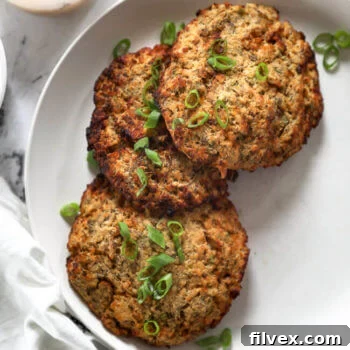 Three air fryer salmon patties on a plate with sliced green onions on top
