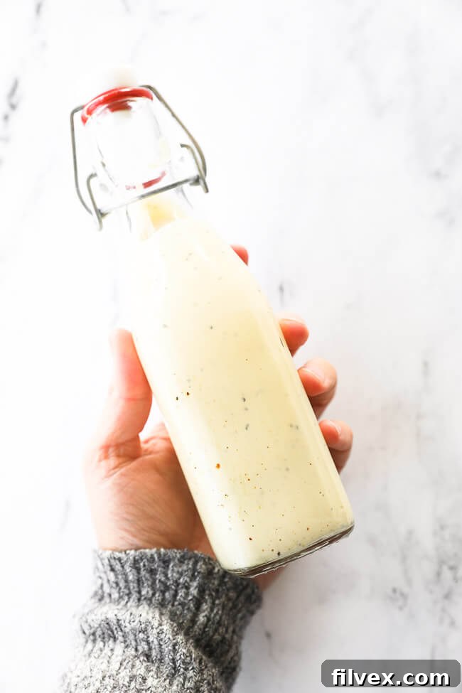 Image of holding a glass dressing jar filled with homemade caesar salad dressing. The rich, creamy texture and inviting golden hue highlight the deliciousness of this low-carb concoction.