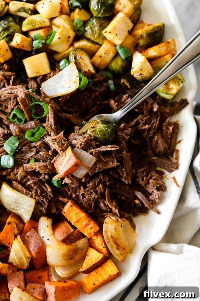Close up overhead shot of shredded slow cooker beef pot roast on a platter with a fork on the side, emphasizing the tender, shreddable texture of the beef and its delicious juices