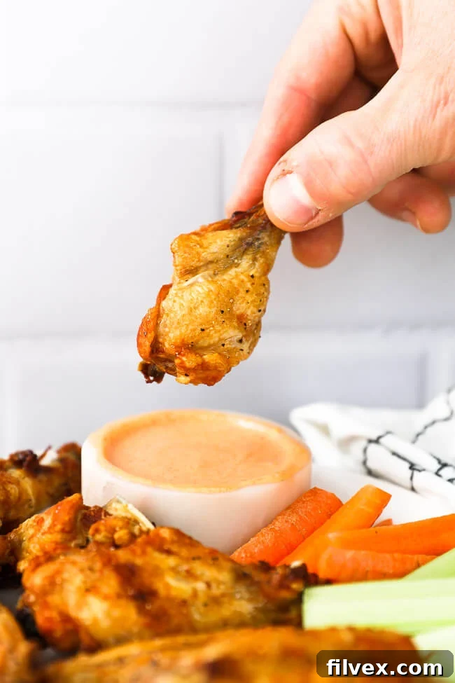 Small chicken drumstick held in a hand over dipping sauce, showcasing crispiness