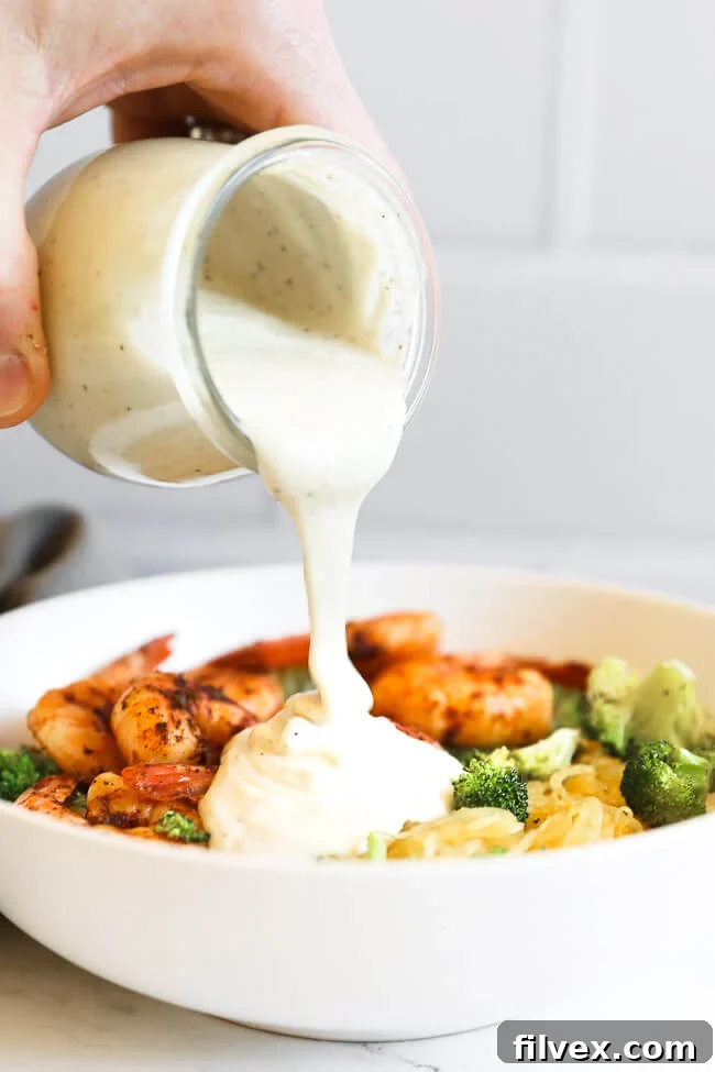 Image of pouring dairy free alfredo sauce into a bowl full of spaghetti squash, shrimp and broccoli to make spaghetti squash alfredo. 