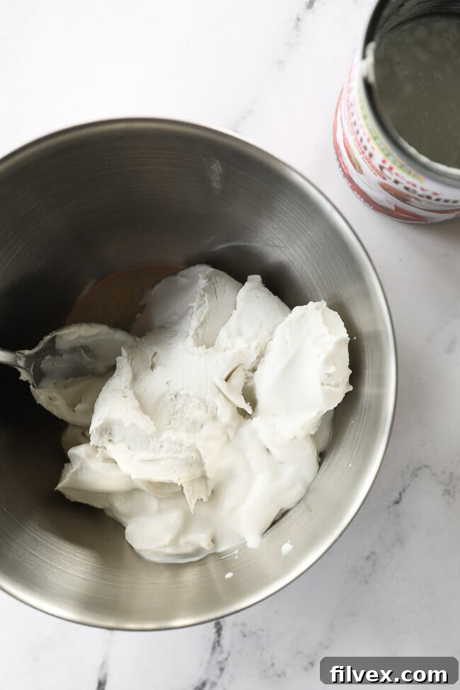Coconut cream scooped out of a can and into a metal bowl with a spoon. 