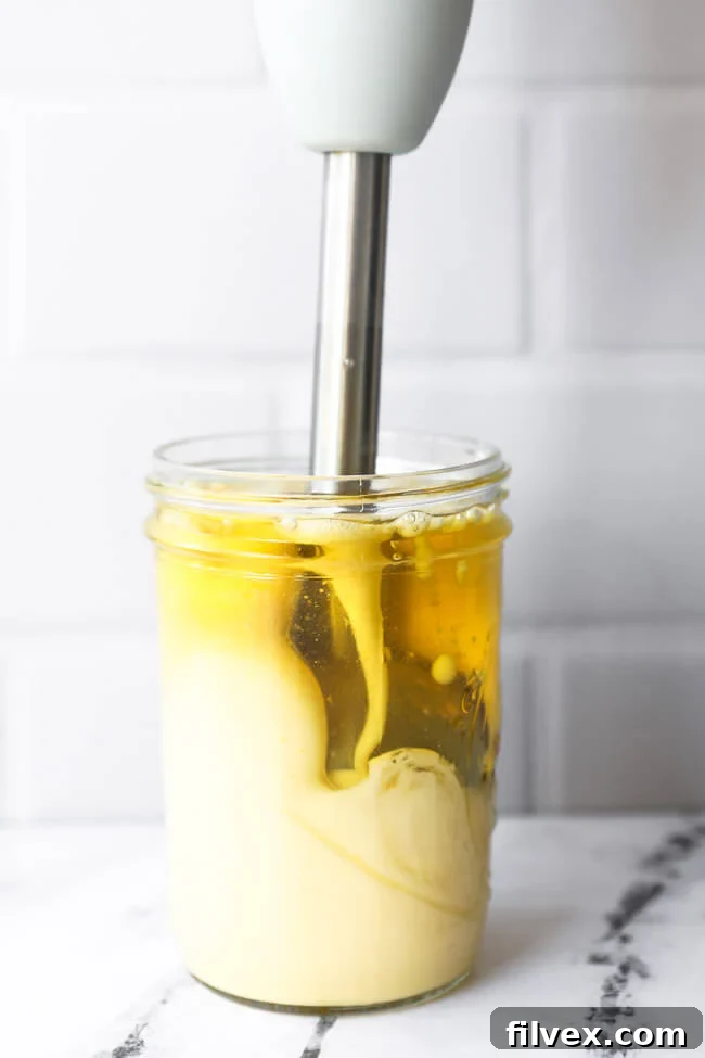Immersion blender actively mixing ingredients in a jar to make homemade mayo, showing the thickening process at the bottom of the jar