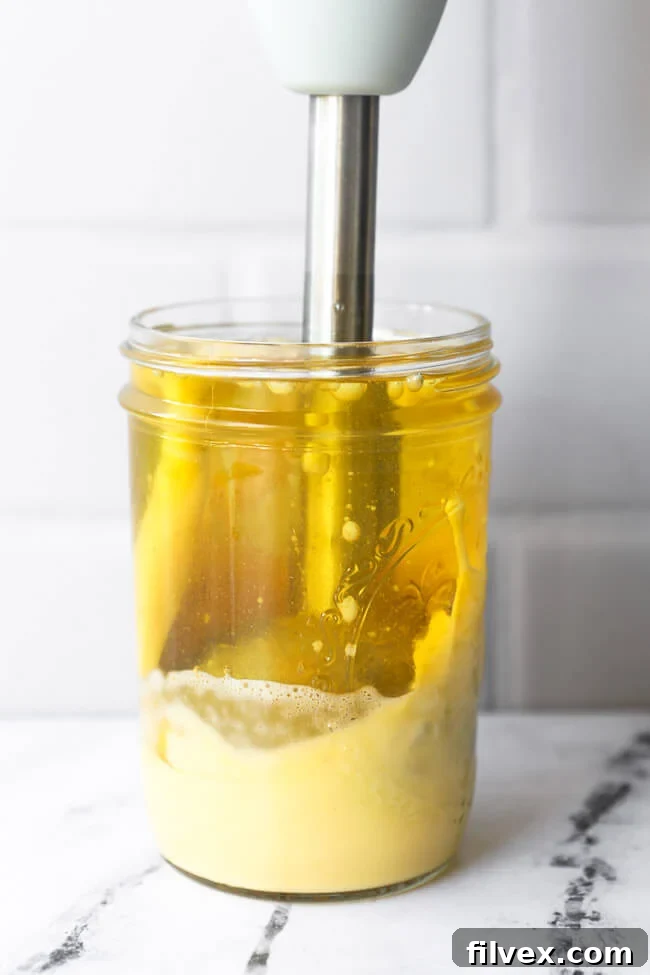 Immersion blender just beginning to emulsify ingredients for homemade mayo, with the bottom visibly thickening into a creamy consistency