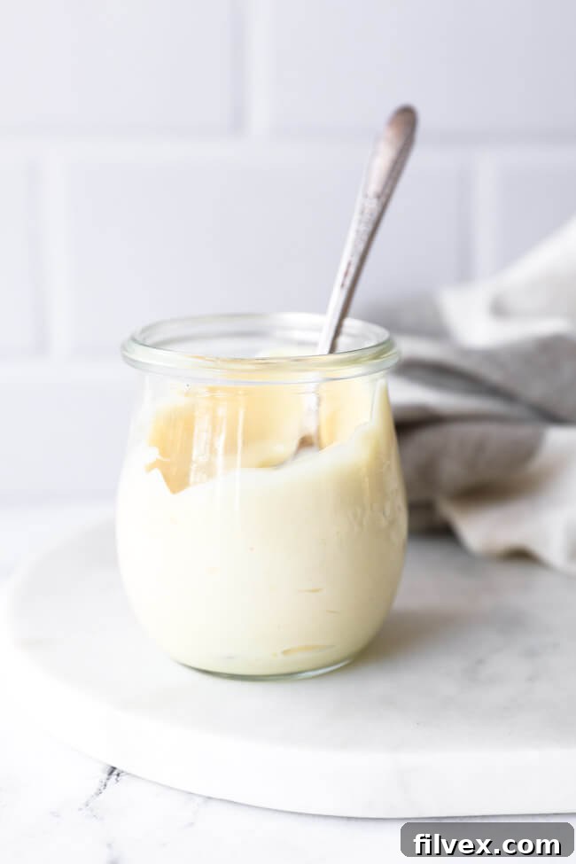 Small round jar of thick, creamy keto mayo with a spoon sticking out, showcasing the perfect texture of homemade quality mayonnaise