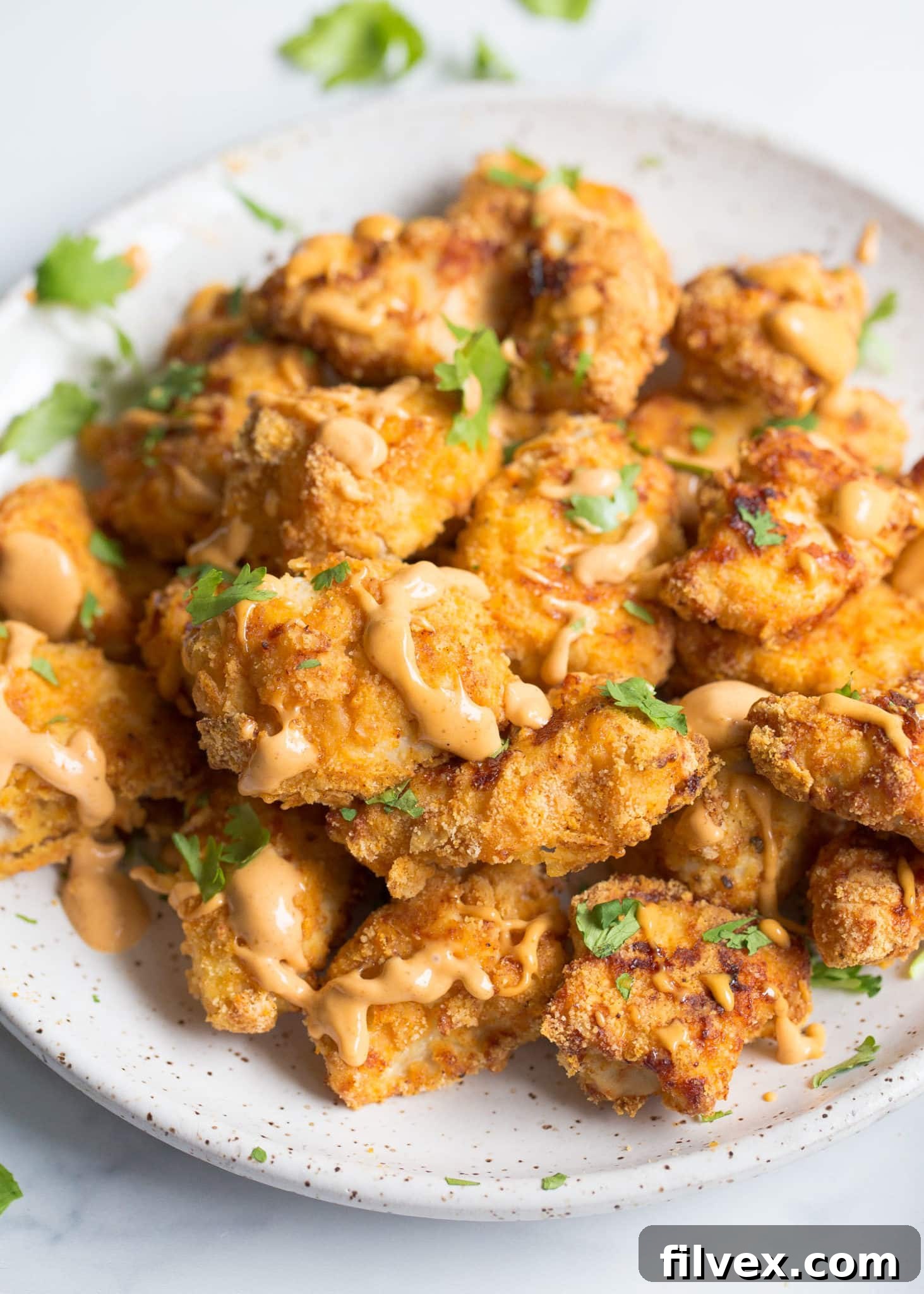 Chicken nuggets on a plate with sauce drizzle and chopped parsley
