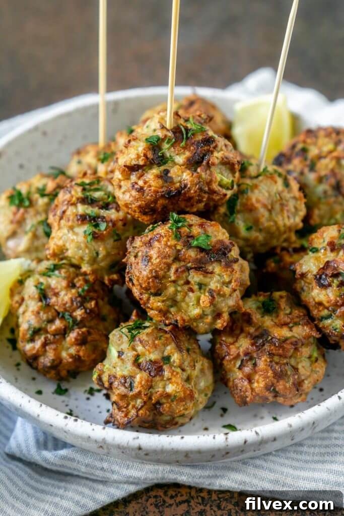 Pile of meatballs on a plate with lemon wedges and skewers in a few meatballs