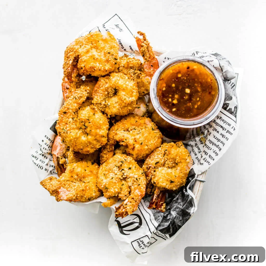 Air fryer shrimp in a newspaper lined basket with chili sauce on the side