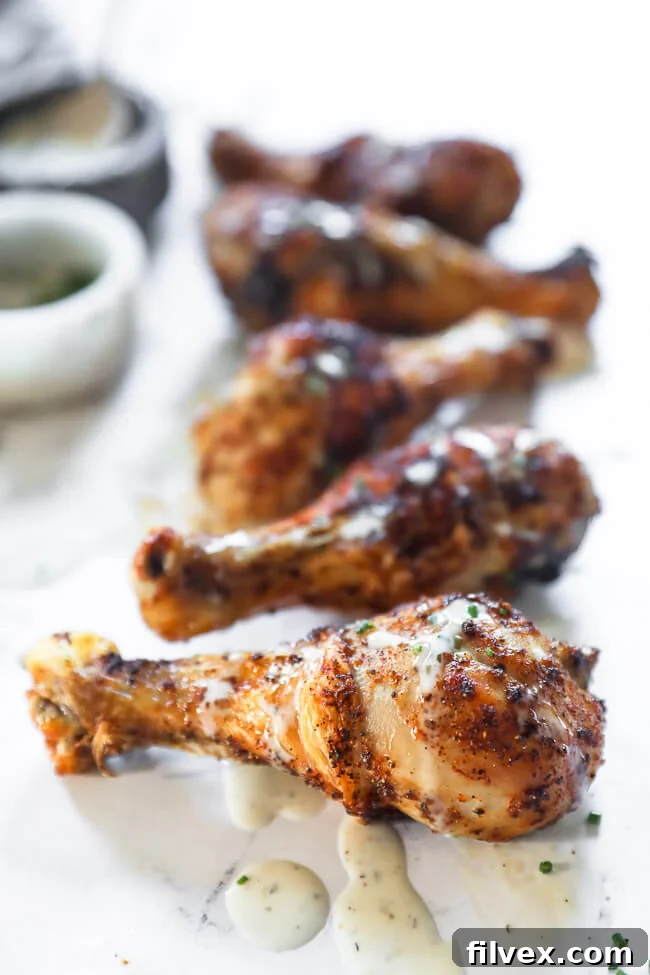 Angled image of chicken drumsticks in a line on marble with ranch drizzled on top. 