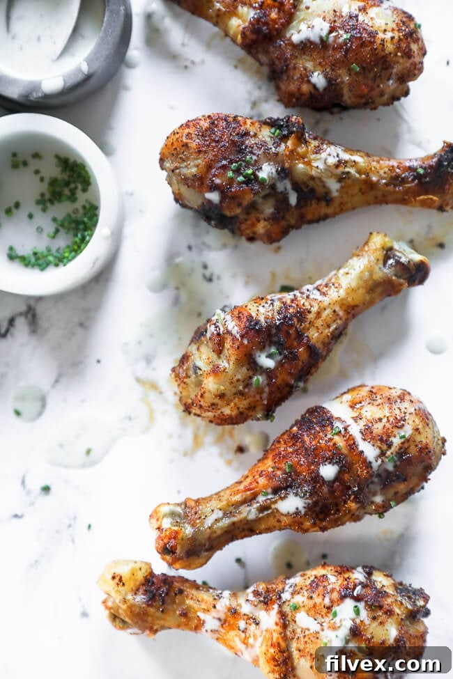 Overhead image of five chicken drumsticks in a line on marble with ranch drizzled on top. 