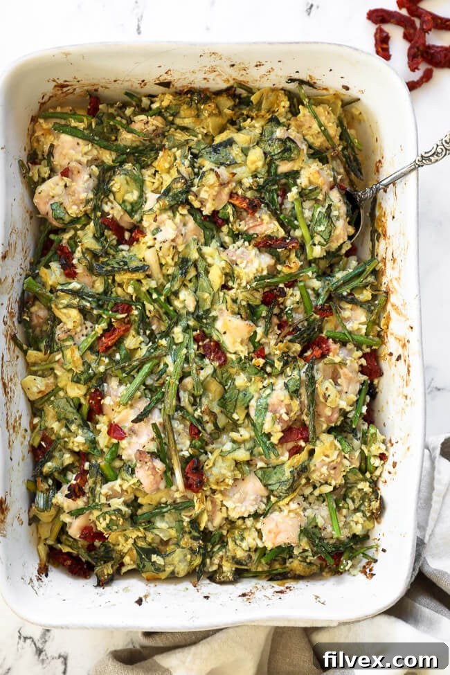 A delectable overhead view of creamy spinach artichoke chicken casserole in a baking dish, with a serving spoon ready to dish out a portion. The golden-brown top hints at its deliciousness.