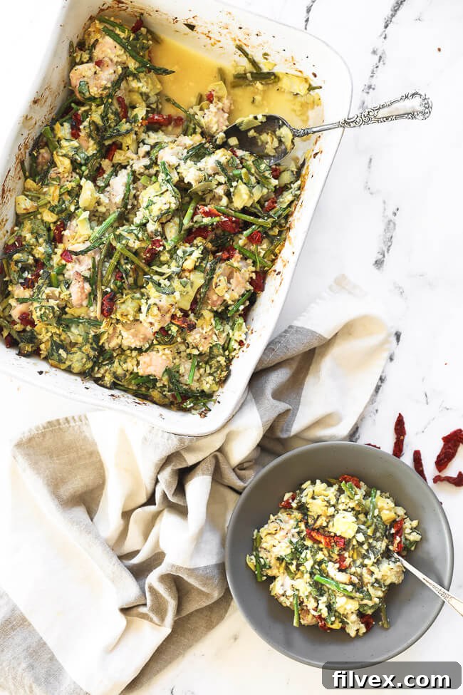 An inviting image of a portion of creamy spinach artichoke chicken casserole served in a bowl, with the main dish still in the casserole pan. Steam subtly rises, indicating its warmth.