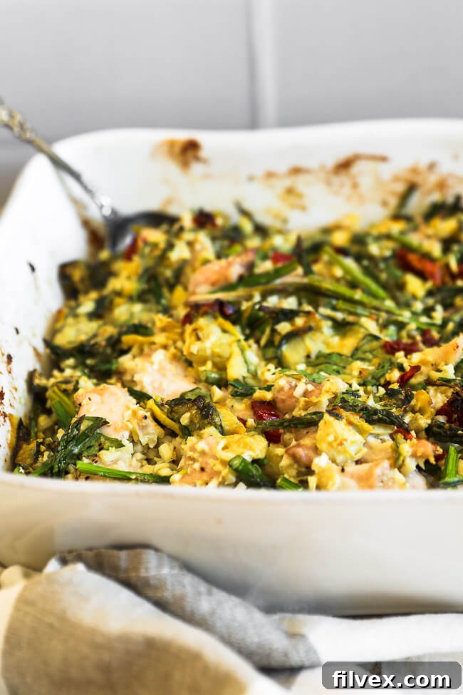 An angled shot revealing the rich texture of the creamy spinach artichoke chicken casserole in its dish, with a serving spoon scooping out a generous portion, showing off the chicken and vegetables.