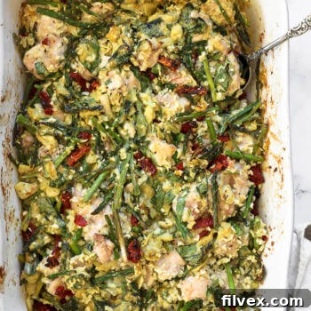 Creamy spinach artichoke chicken casserole in a casserole dish with a serving spoon dug in.