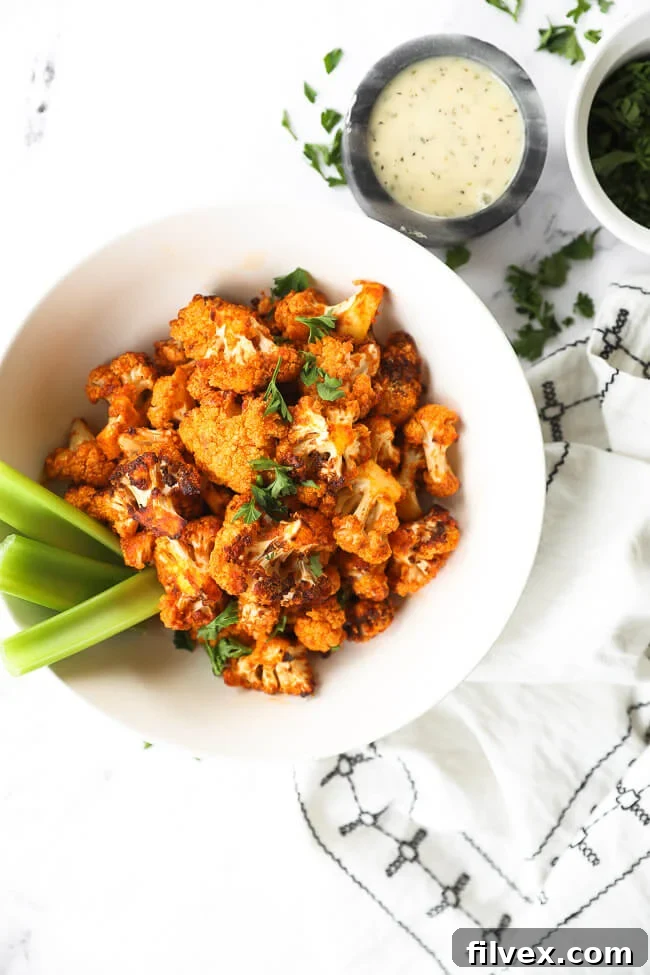 buffalo cauliflower bites in a bowl with celery sticks and ranch dressing on the side