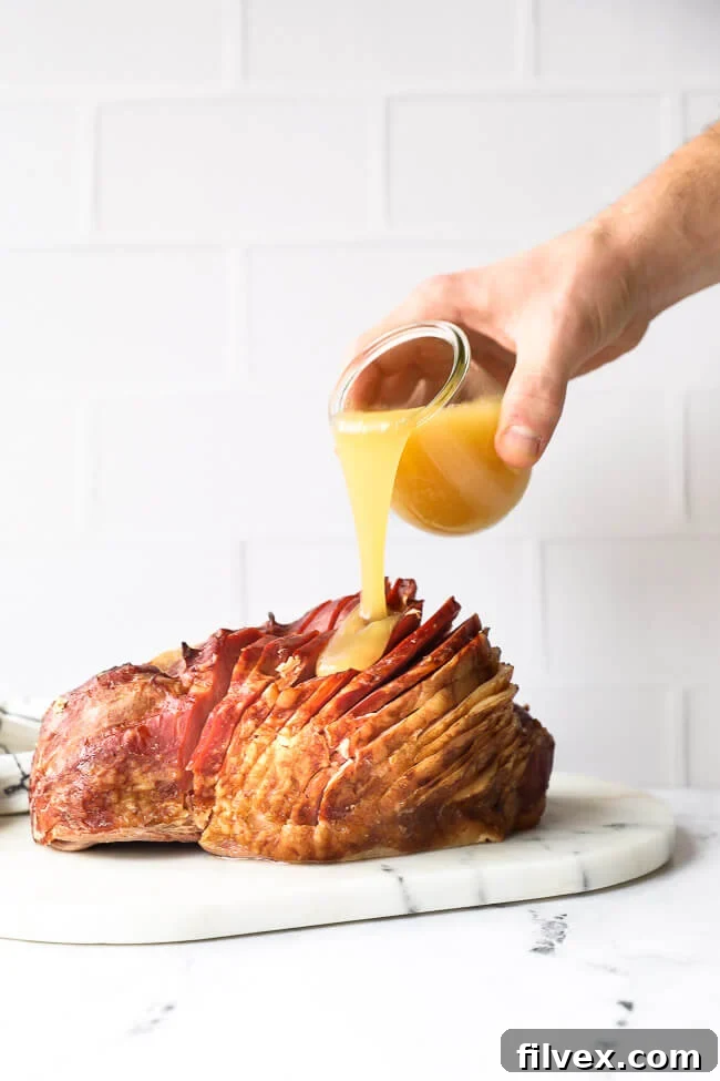 Straight on shot of sliced whole ham with hand pouring honey glaze over the top