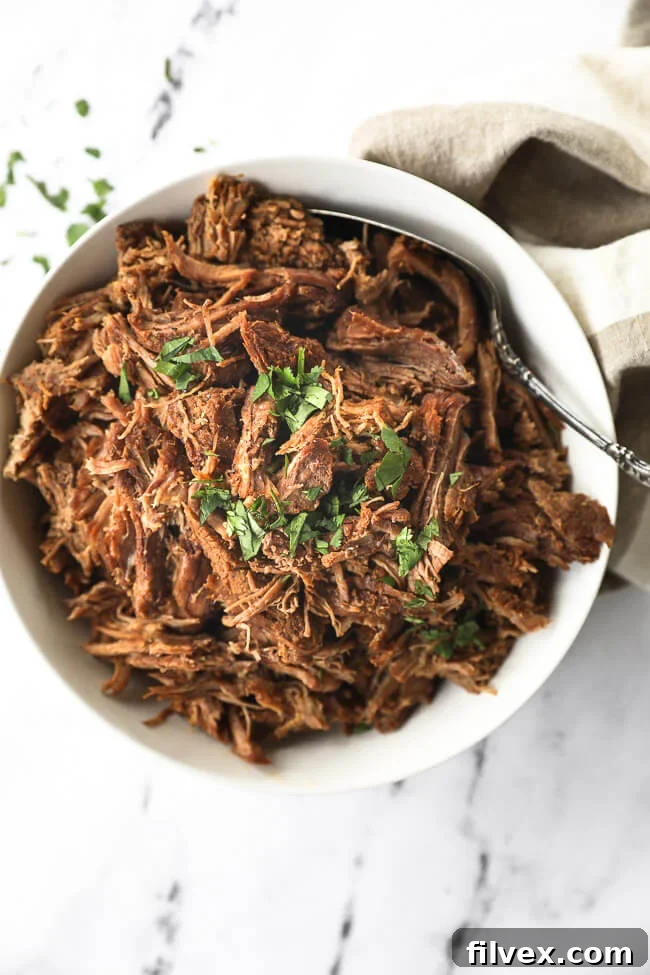 Instant pot shredded beef in a white bowl with chopped parsley topping