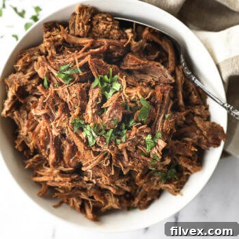 Instant pot shredded beef in a white bowl with chopped parsley topping
