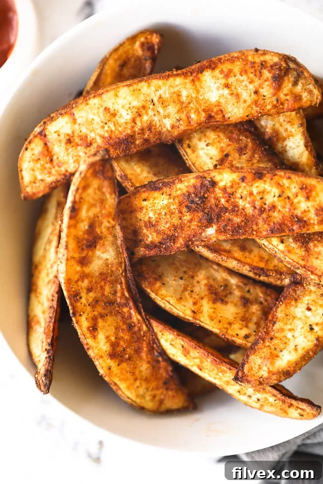Vertical close up overhead image of air fryer potato wedges piled in a bowl. 