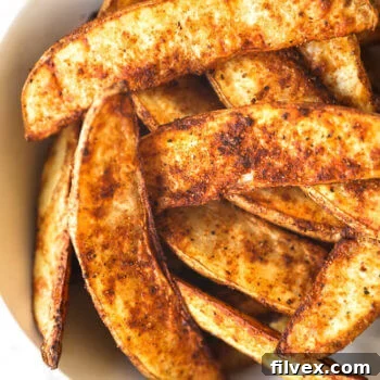 Close up image of air fryer potato wedges in a bowl. You can see the crispy edges and seasonings.