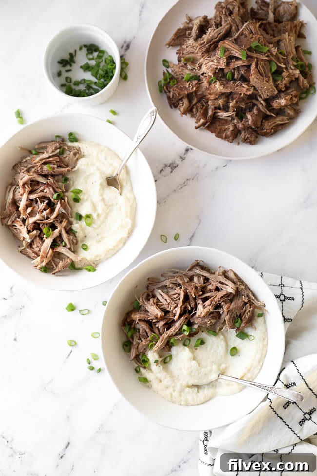 Two bowls of mashed cauliflower and instant pot pork shoulder with green onion on top and forks dug into bowl. Side of extra pulled pork on a plate. 