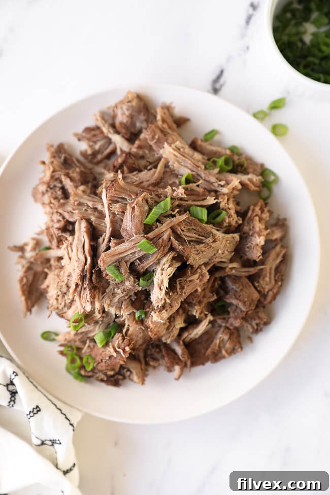 Overhead image of instant pot pulled pork piled on a plate with with chopped green onion on top. 