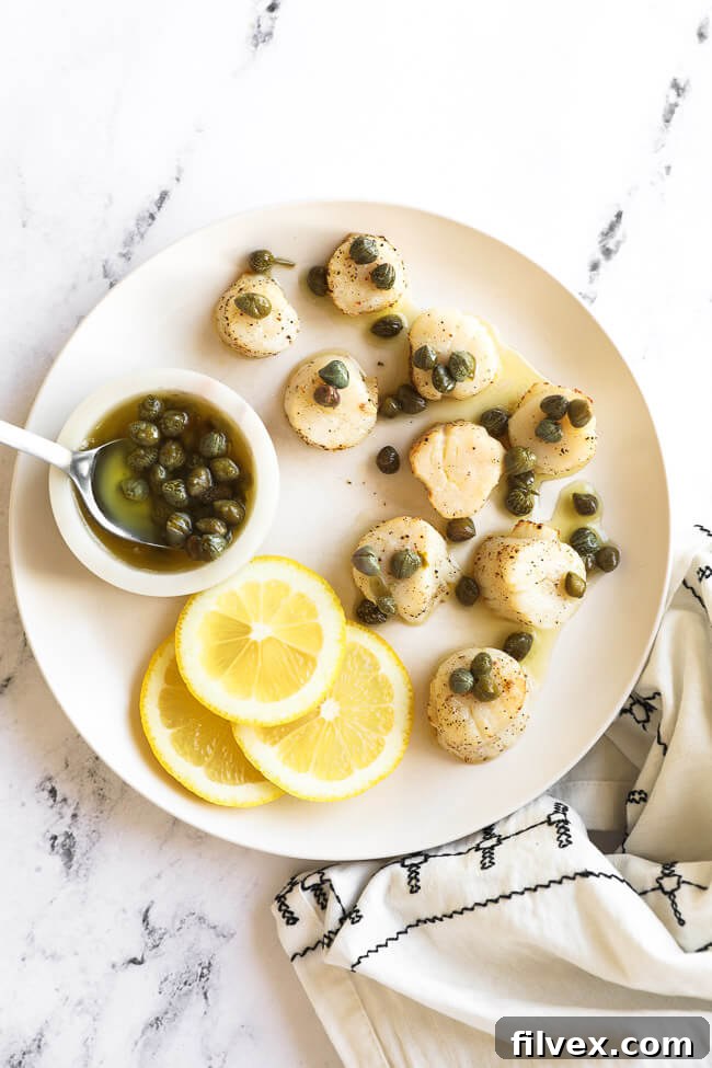 Air fryer scallops on a white plate with butter sauce and capers on top. Lemon slices and capers in the side.