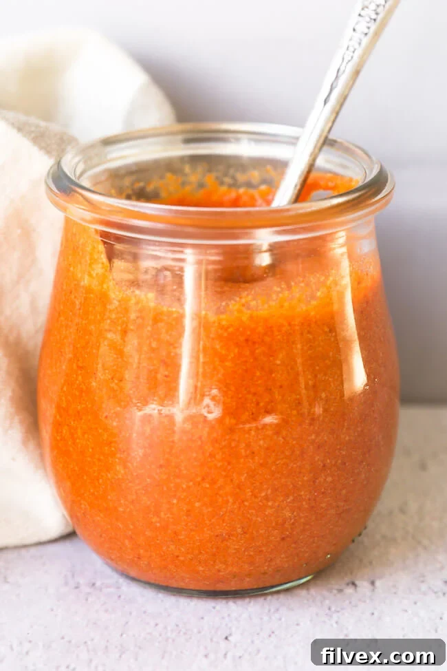 Homemade keto buffalo sauce in a small jar with spoon coming out, showcasing its thick and tangy texture.
