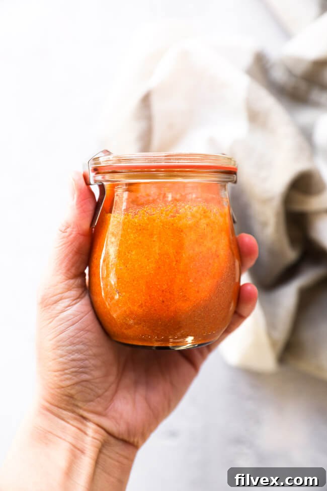 Hand holding up a jar of keto buffalo sauce - overhead shot. Perfect for storing this delicious homemade condiment in your fridge.